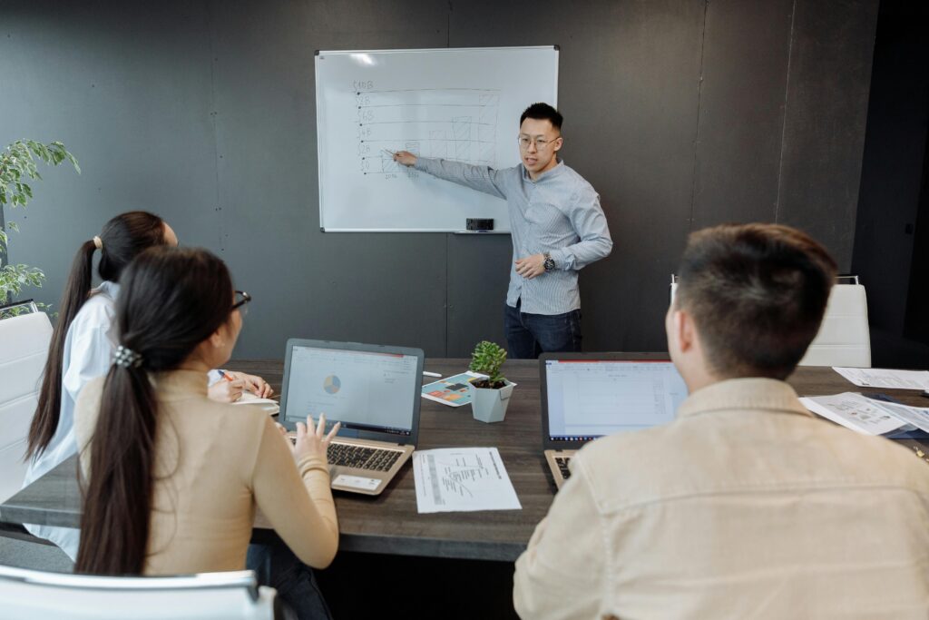 A group of sales professionals in a meeting while a team leader presents a strategy on a whiteboard